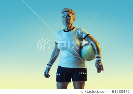 Senior woman training in volleyball in sportwear on gradient background in neon light Senior woman training in volleyball in sportwear on gradient background in neon light 61280471