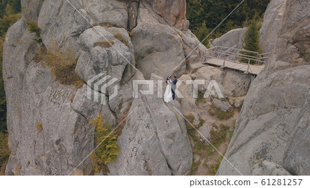 Newlyweds stand on a high slope of the mountain. Groom and bride. Aerial view 61281257