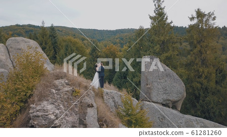 Newlyweds stand on a high slope of the mountain. Groom and bride. Aerial view 61281260