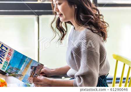 A woman planning a trip by the window (Travel brochure is a dummy created for shooting.) 61290046