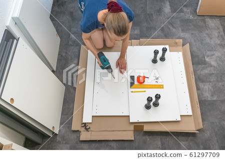 Female with a cordless driver collects furniture. Female with a cordless driver collects furniture. 61297709