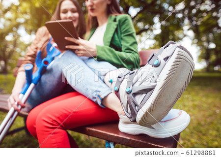 Two best friends, one with an injured leg, reading a book Two best friends, one with an injured leg, reading a book 61298881