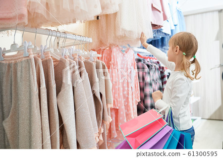 Little customer standing in store and choosing new dresses 61300595
