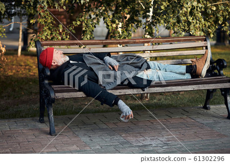 Vagabond male sleeping on bench during the day 61302296