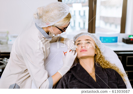 Young woman cosmetologist performs the botox procedure in the clinic to beautiful blond woman. Cosmetology. Beauty Face 61303087