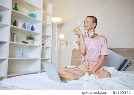 Pretty caucasian woman watching on laptop while having a cup of tea on white bed Pretty caucasian woman watching on laptop while having a cup of tea on white bed 61305543