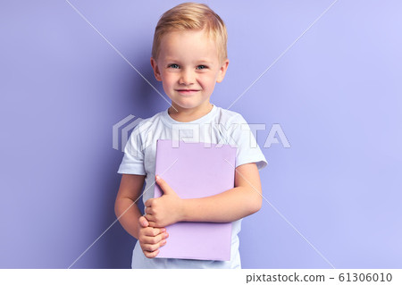 Little shy boy holding book isolated on purple background 61306010