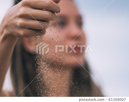 Young woman with dreadlocks pouring sand Young woman with dreadlocks pouring sand 61308007