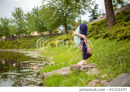 A young sports girl practices yoga on a green lawn A young sports girl practices yoga on a green lawn 61310397