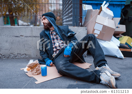 Dirty beggar with food sitting at the trashcan 61311213