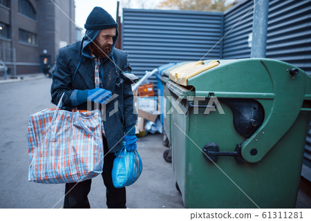 Male bearded beggar searching food in trashcan Male bearded beggar searching food in trashcan 61311281