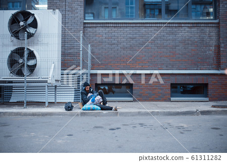 Male bearded beggar eats on city street 61311282