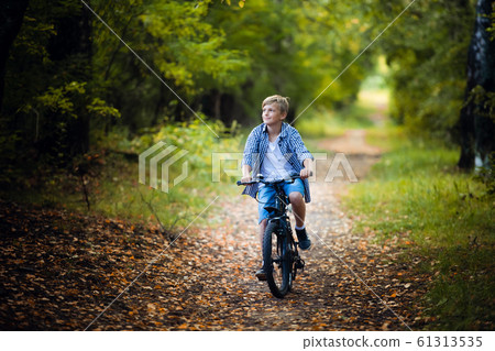 Teen boy rides a bicycle along a path in the forest. The cyclist rides fast through the springboards. Teen boy rides a bicycle along a path in the forest. The cyclist rides fast through the springboards. 61313535