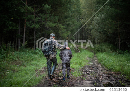 Hunters with hunting equipment going away through rural field towards forest at sunset during hunting season in countryside. Hunters with hunting equipment going away through rural field towards forest at sunset during hunting season in countryside. 61313660