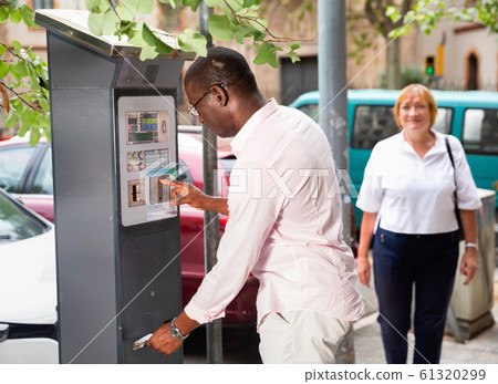 Positive African American man buying ticket for street parking in modern parking meter 61320299