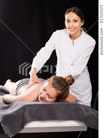 female masseur doing massage at back young woman, who lying on a massage table in a beauty salon 61320325