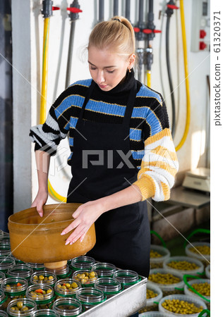 Workwoman filling glass jars with pickled olives Workwoman filling glass jars with pickled olives 61320371