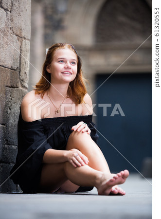 Cheerful girl sitting barefoot near the brick wall Cheerful girl sitting barefoot near the brick wall 61320553