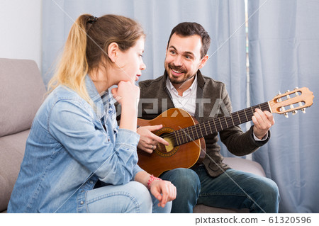 Male tutor assisting teenage pupil in learning how to play guitar 61320596