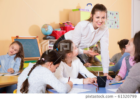 Group of school kids with pens and notebooks studying in classroom with teacher Group of school kids with pens and notebooks studying in classroom with teacher 61320799