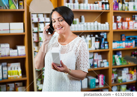 Woman chatting by phone while shopping in drugstore 61320801