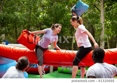 Women fighting by pillows on inflatable beam 61320888