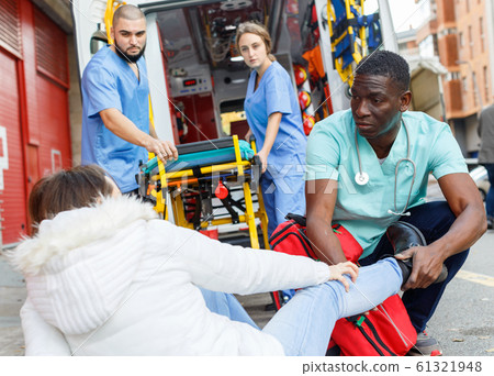 Paramedics providing first aid to injured woman near ambulance car 61321948