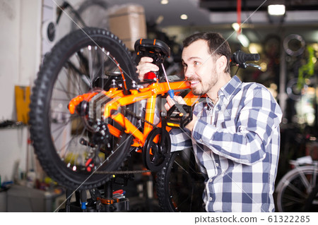 Man in sports workshop mounts bike using special tools Man in sports workshop mounts bike using special tools 61322285