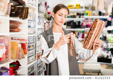 Interested young woman choosing colorful ribbons and braid for dressmaking in sewing supplies shop Interested young woman choosing colorful ribbons and braid for dressmaking in sewing supplies shop 61322315