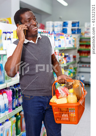 Positive afro man using his smartphone while shopping in supermarket Positive afro man using his smartphone while shopping in supermarket 61322321