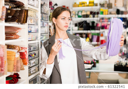 Interested young woman choosing colorful ribbons and braid for dressmaking in sewing supplies shop Interested young woman choosing colorful ribbons and braid for dressmaking in sewing supplies shop 61322541