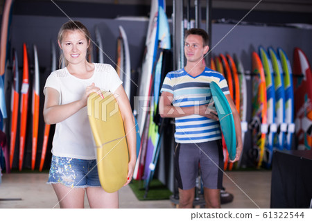 Positive woman surfer holding surfboard in store 61322544