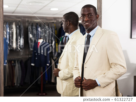 Portrait of male client choosing classic beige jacket in the mall Portrait of male client choosing classic beige jacket in the mall 61322727