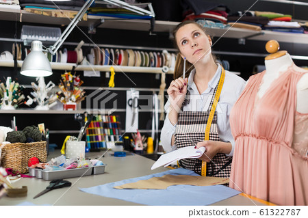 Female seamstress is thinking about new dress for collection of clothes Female seamstress is thinking about new dress for collection of clothes 61322787