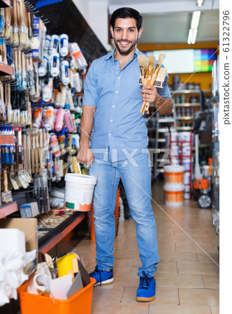 Man standing amongst racks in paint store with brushes and paint Man standing amongst racks in paint store with brushes and paint 61322796