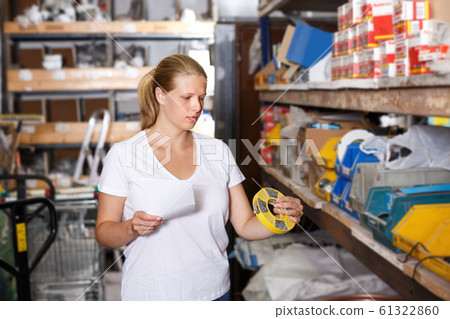 Woman customer holding shop list and looking tools at shelves 61322860