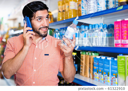 Man is choosing water with help mobile in supermarket. Man is choosing water with help mobile in supermarket. 61322910