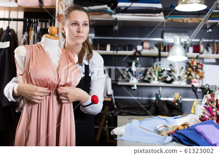Female seamstress is thinking about new dress for collection of clothes near mannequin Female seamstress is thinking about new dress for collection of clothes near mannequin 61323002