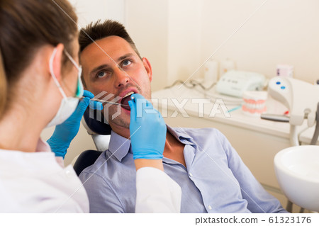 Orthodontist in uniform is taking visional inspection of a young male Orthodontist in uniform is taking visional inspection of a young male 61323176