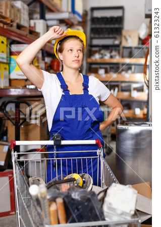 Young female worker in uniform and helmet with basket of construction materials in the build store Young female worker in uniform and helmet with basket of construction materials in the build store 61323243