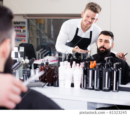 Young guy stylist demonstrating final haircut to client at hairdressing salon Young guy stylist demonstrating final haircut to client at hairdressing salon 61323245