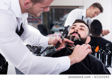 Adult guy creating shape for beard of client 61323291
