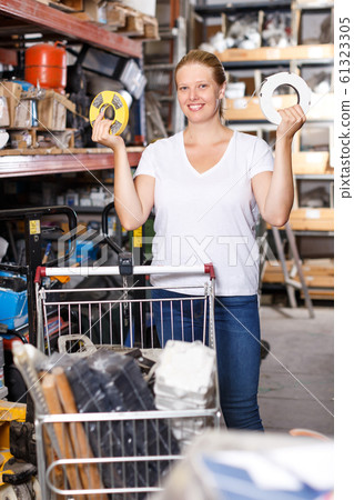 Young woman customer with basket looking construction materials in store Young woman customer with basket looking construction materials in store 61323305
