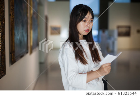 Chinese female visitor with guide-book looking at artwork painting 61323544