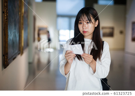 Chinese woman standing with guide-book near painting in baguette Chinese woman standing with guide-book near painting in baguette 61323725