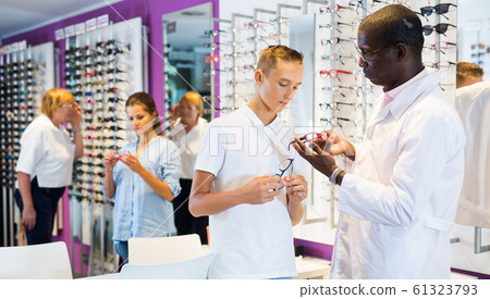 Professional male optician helping client to choose a spectacles Professional male optician helping client to choose a spectacles 61323793