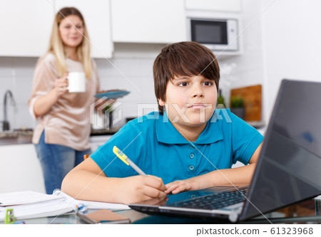 Boy doing homework, mother cooking 61323968
