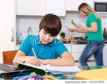 Boy doing homework, mother cooking Boy doing homework, mother cooking 61323973