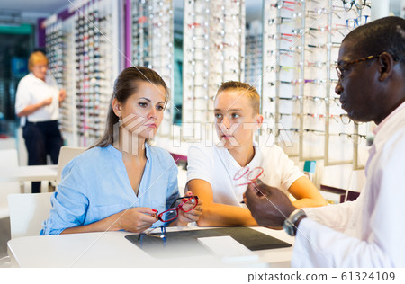 Optometrist helping mother to choose glasses for teen son 61324109