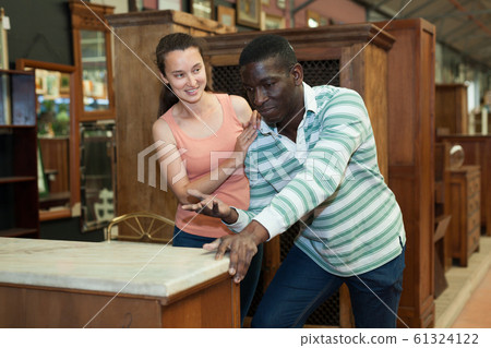 Man with girlfriend searching wooden pieces of furniture in store 61324122